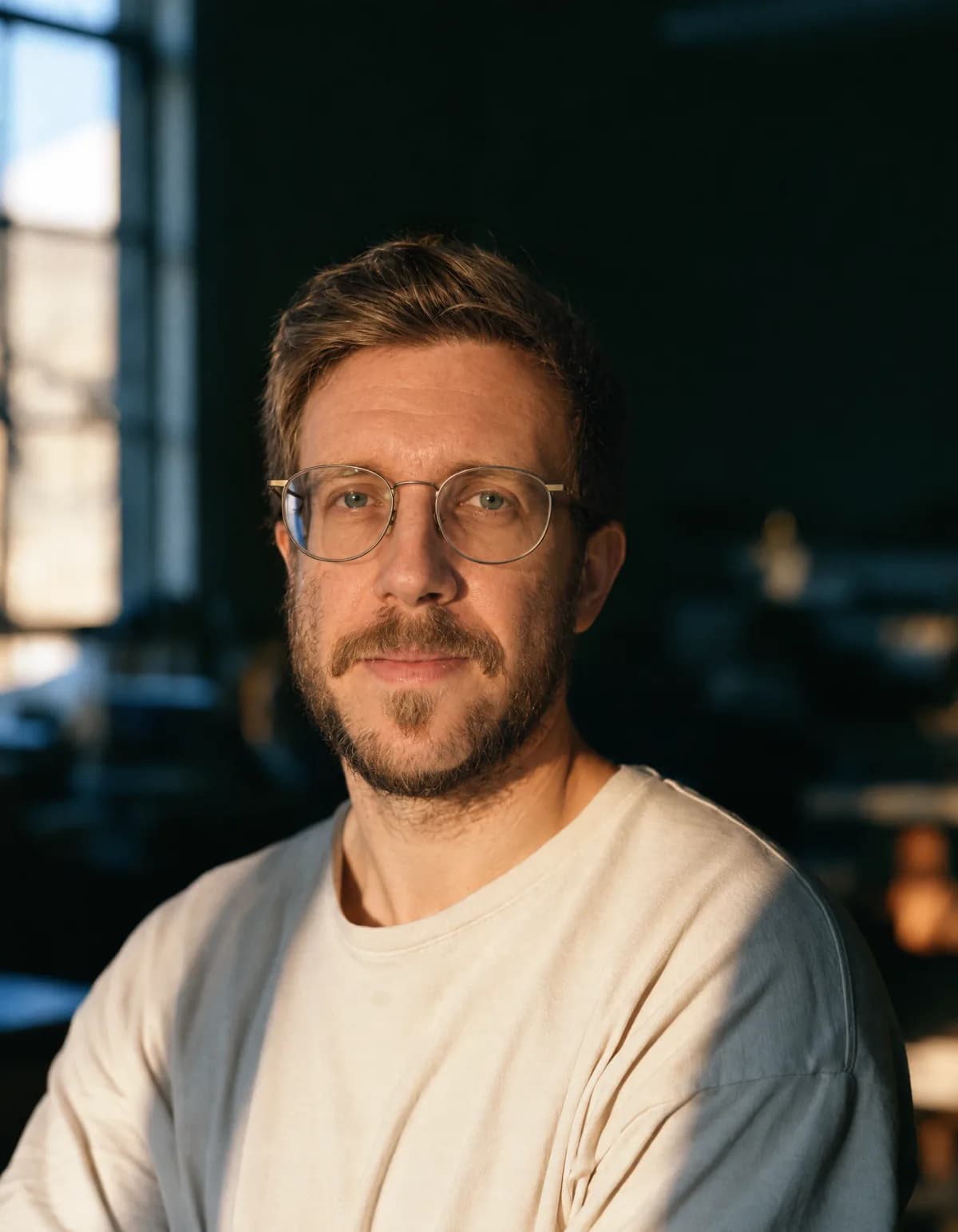 Philipp Russner — Portrait in einer Werkstatt, Brille, helles Shirt, von der Seite durch ein Fenster beleuchtet